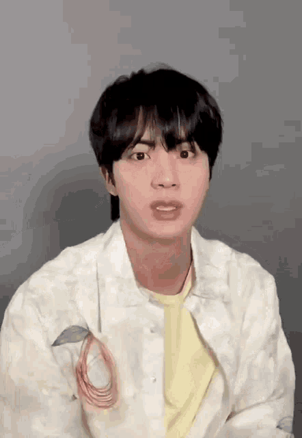 a young man wearing a white jacket and a yellow t-shirt is making a funny face .