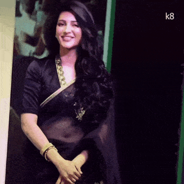 a woman in a black saree is standing in front of a sign that says k8 on it