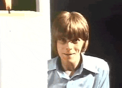 a young man in a blue shirt is standing in a doorway .