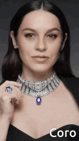 a woman is wearing a necklace and a ring with a blue stone pendant .