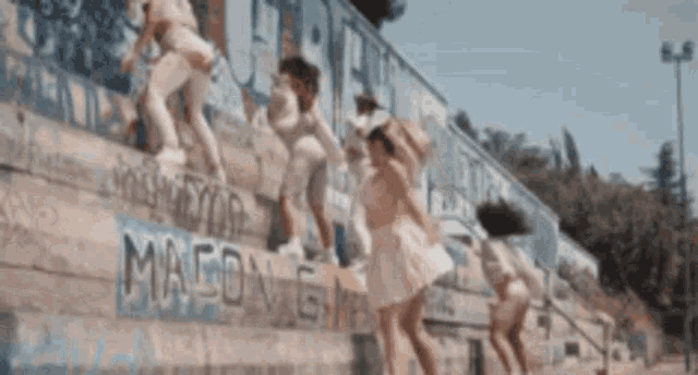 a group of young women are jumping on a wall with graffiti on it .