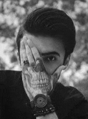 a man with a tattoo of a skull on his hand is covering his face with his hand .