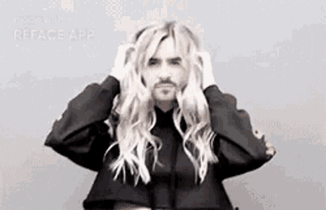 a man with long blonde hair and a beard is wearing a black shirt and holding his hair .