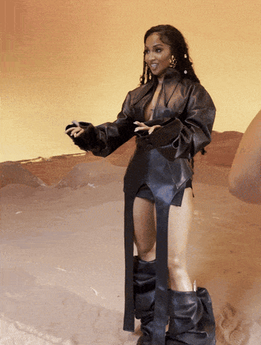 a woman in a black leather outfit is standing in a desert