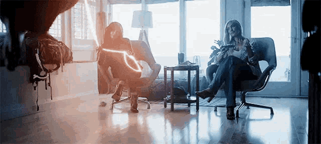 two women are sitting in chairs in a living room with a light coming out of the ceiling .