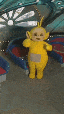 a yellow teletubbies doll is standing in front of a carousel .