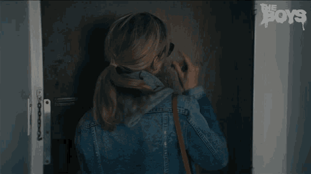 a woman in a denim jacket stands in front of a wall that says the boys on it