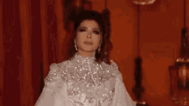 a woman in a white dress is standing in a room with a red curtain .