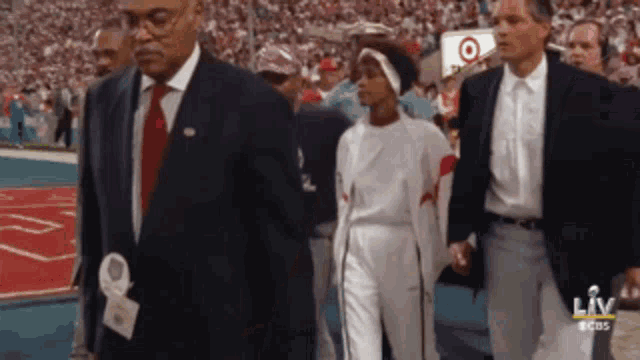a man in a suit and tie walks with a woman in white pants in front of a sign that says liv on it