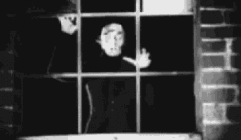 a black and white photo of a man looking out of a window