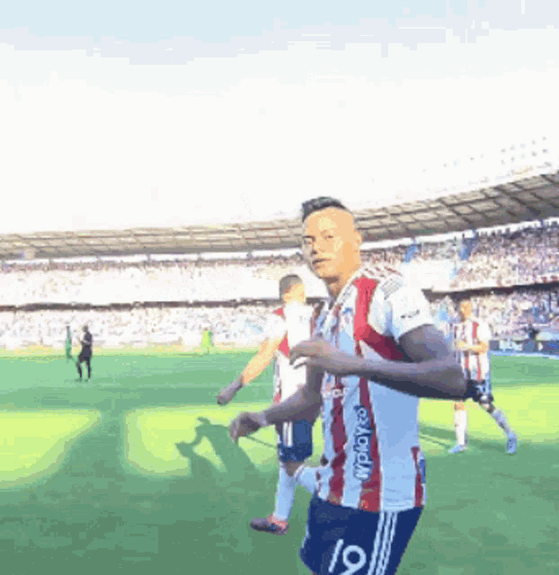 a man in a red and white striped jersey with the number 19 on the shorts is running on a soccer field