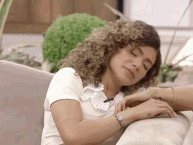 a woman with curly hair is laying on a couch with her eyes closed and a watch on her wrist