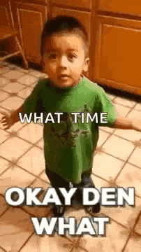 a little boy in a green shirt is standing on a tiled floor in a kitchen .