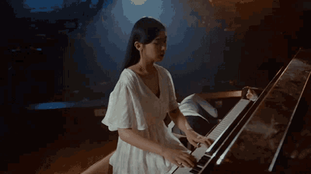 a woman in a white dress plays a piano