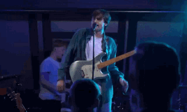 a man singing into a microphone while playing a guitar that says fender on it