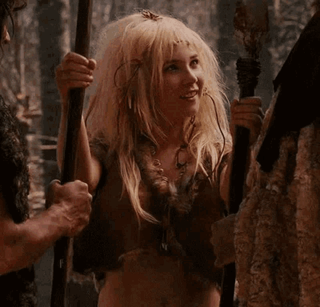 a woman with blonde hair is standing next to a man holding a spear and smiling .