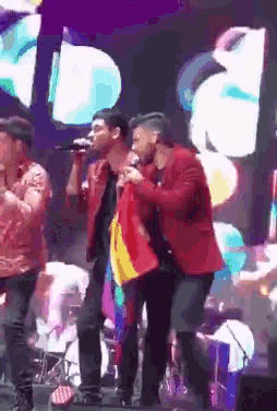 a man in a red jacket is holding a rainbow flag while singing into a microphone