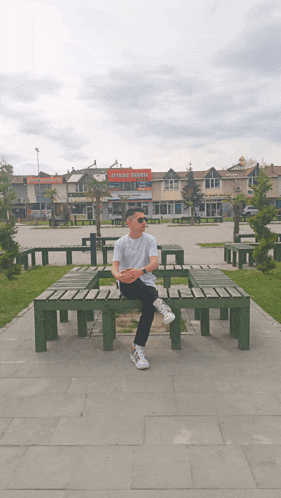 a man sits on a wooden bench in front of a store called ataköy sebze