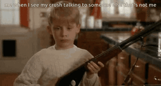 a young boy is holding a shotgun in a kitchen with a caption that says me when i see my crush talking