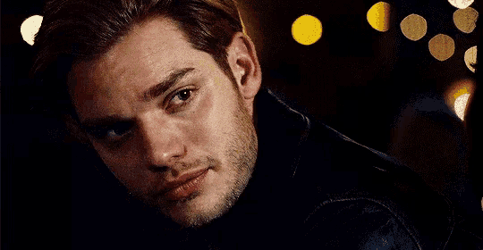 a close up of a man 's face with his eyes closed in a dark room with lights in the background .
