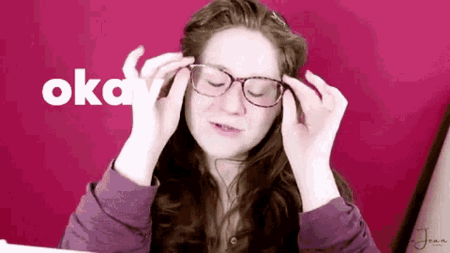 a woman adjusts her glasses in front of a red background that says okay