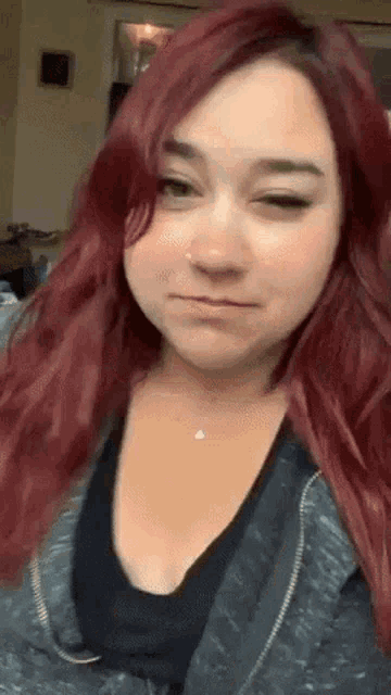 a woman with red hair is making a funny face while wearing a black shirt and a grey jacket .