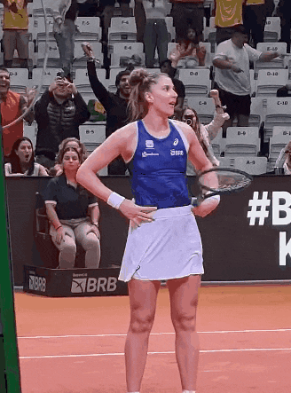 a woman is holding a tennis racquet on a court with a brb sign in the background