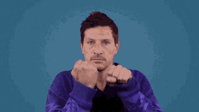 a man in a purple sweater is making a fist gesture