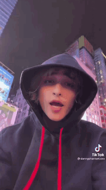 a man wearing a black hoodie with a red ribbon around his neck is smiling for the camera .