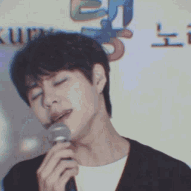 a young man is singing into a microphone with his eyes closed and his mouth open .