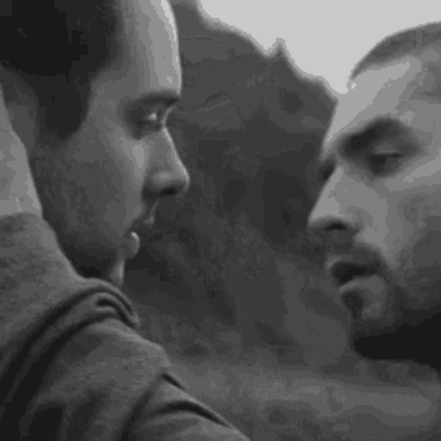 a couple of men are kissing in a black and white photo .