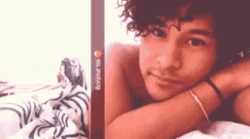 a man with curly hair is laying on a bed with his head on his arm .