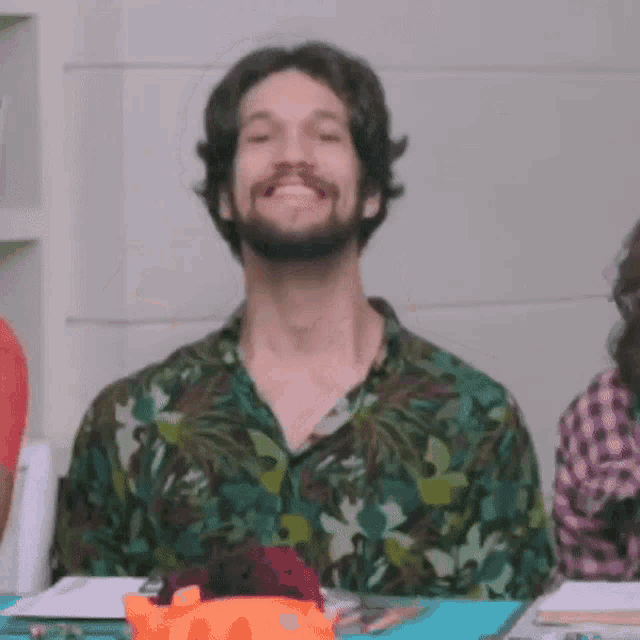 a man with a beard is smiling and sitting at a table .