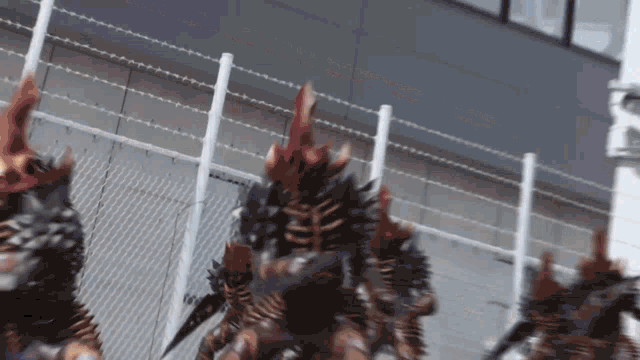 a group of monsters are standing next to a barbed wire fence in front of a building .