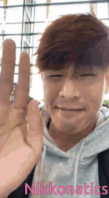 a man with his eyes closed is waving his hand in front of a sign that says nikkonatics