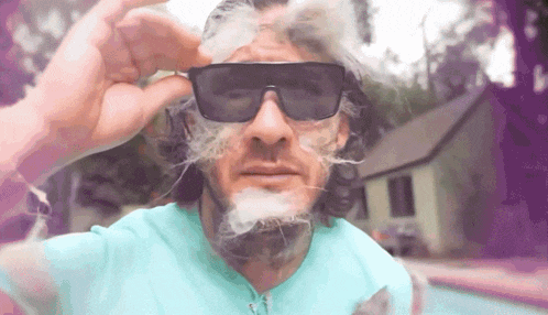 a man wearing sunglasses is blowing smoke out of his mouth