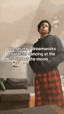 a man is standing in a living room wearing plaid pajamas and a black hoodie .