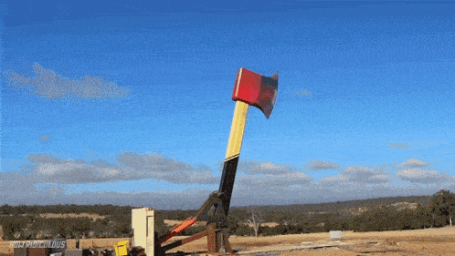 a large red and yellow axe is being thrown in a field with a blue sky in the background