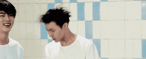 two young men are standing next to each other in front of a tiled wall .