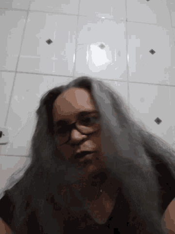 a woman with long hair and glasses is standing in front of a white tiled wall