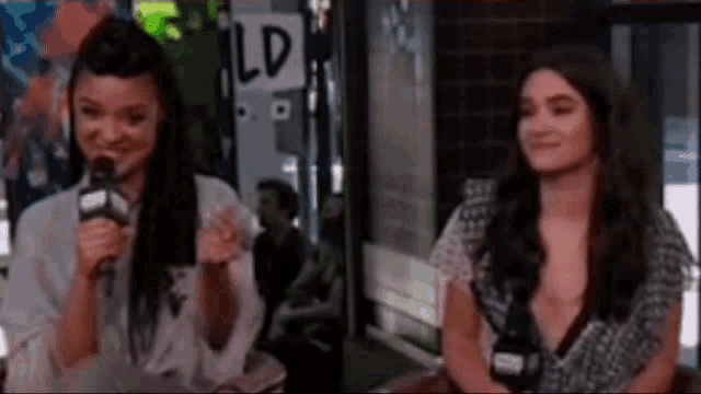 a woman is talking into a microphone while another woman looks on .
