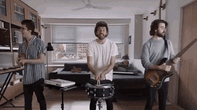 three men are playing instruments in a living room including a drummer and a guitar player