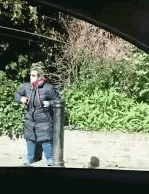 a woman in a black coat is standing next to a post