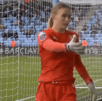 a female soccer player giving a thumbs up in front of a barclays ad