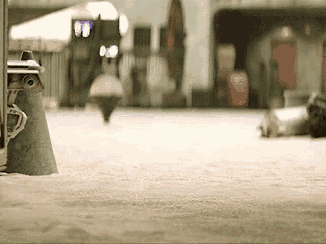 a robot is standing on a sandy surface in front of a building in a city .