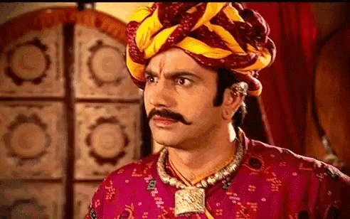 a man with a mustache and a turban is wearing a red shirt and a yellow turban .
