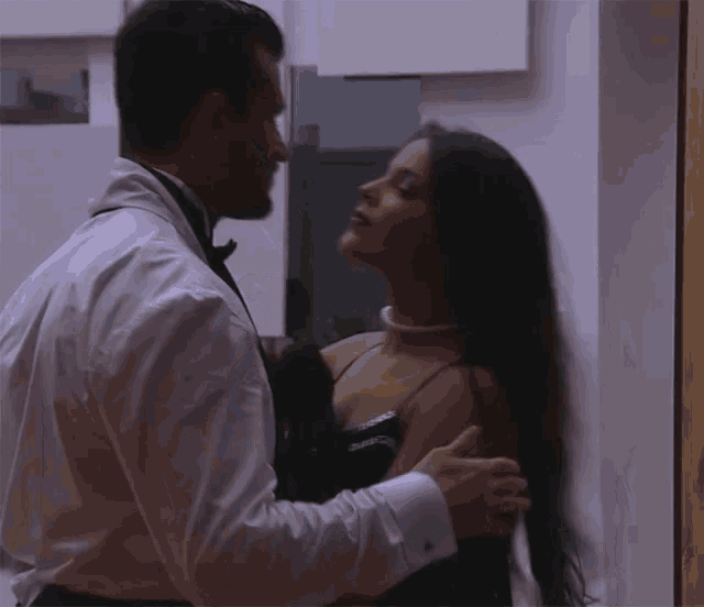 a man in a tuxedo and tie is kissing a woman in a black dress