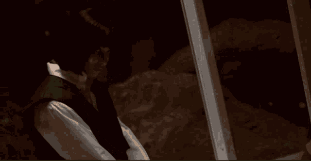 a man in a black vest and white shirt is standing in a dark room