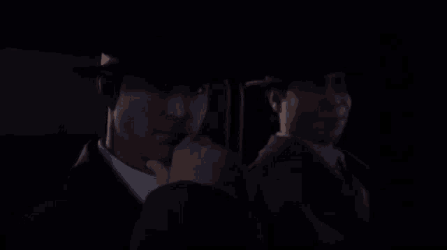 a man in a suit and hat is looking at his reflection in a mirror