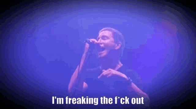 a man is singing into a microphone with the words `` i 'm freaking the f ck out '' behind him .